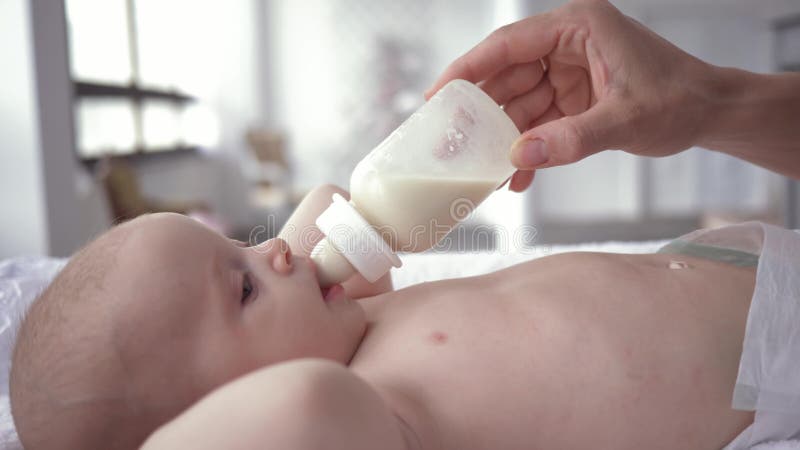 Porträt von Trinkmilch des Babys von einer Flasche, dass Muttergriffe in ihren Händen, die in der Windel neugeboren sind, auf dem