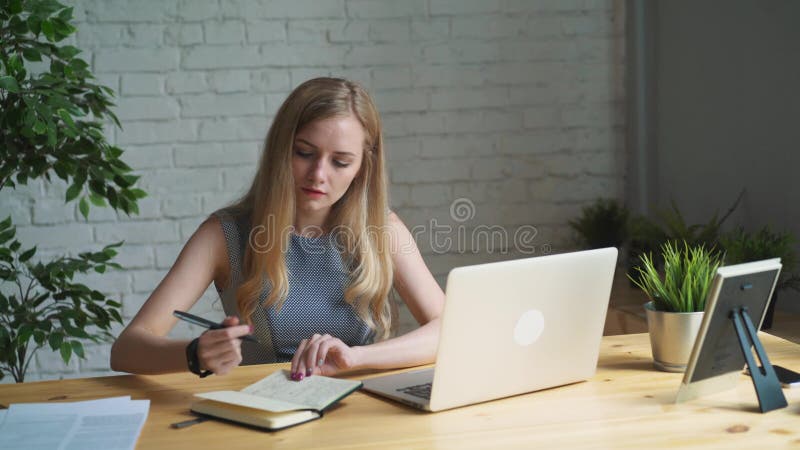 Porträtaufnahme einer kreativen Frau, die an ihrem Schreibtisch sitzt Unter Verwendung des Notizbuches Sie sitzt in einem Licht u