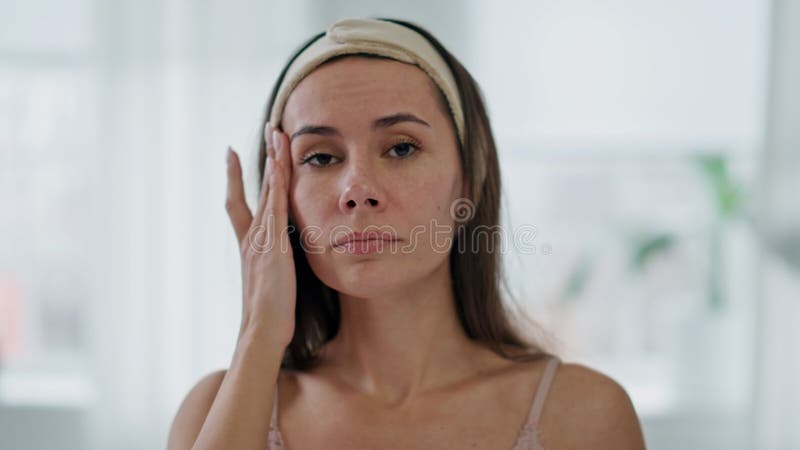 Porträtmüde Frau, die die Haut im Badezimmer berührt. Unglückliche Dame, die Falten überprüft