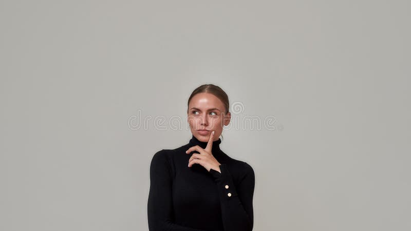 Porträtt av drömmisk kaukasisk ung kvinna som bär svart turtleneck-finger nära ansiktet och ser tankfull ut åt sidan fotografering för bildbyråer