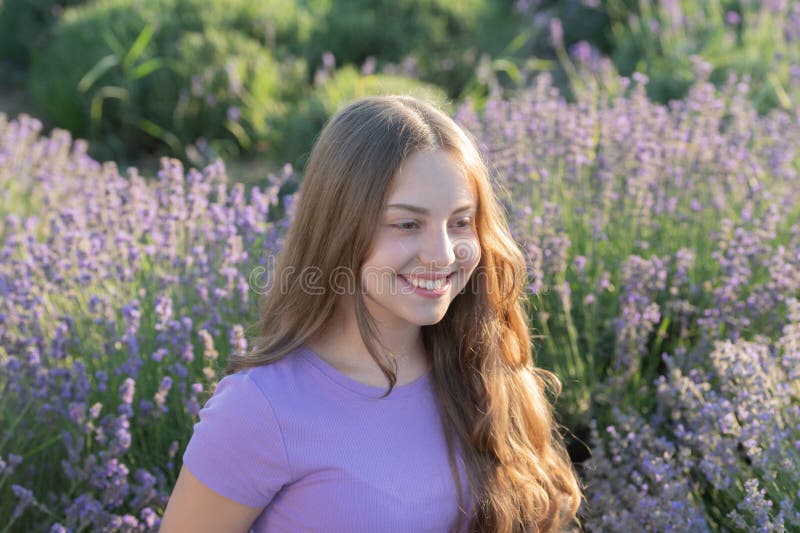 Porträtt av en glad ung flicka med långt hår i ett lavendelfält. tjej som njuter av blomning i lavenderfält. vacker flicka