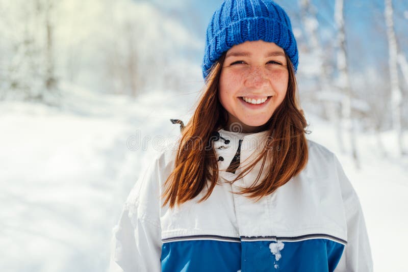 Porträtt av en tonårig flicka i en blå vintersportdräkt på en bakgrund av snöträd