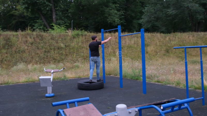 Porträtt av en ung man som gör trupper på den horisontella baren utomhus på en gatulekplats en stark idrottsman arkivfilmer