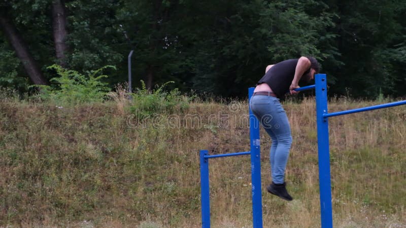 Porträtt av en ung man som gör trupper på den horisontella baren utomhus på en gatulekplats en stark idrottsman arkivfilmer