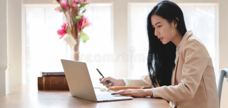 Porträtt av en ung, vacker affärskvinna som arbetar med sitt projekt med en bärbar dator på ett bekvämt kontor fotografering för bildbyråer