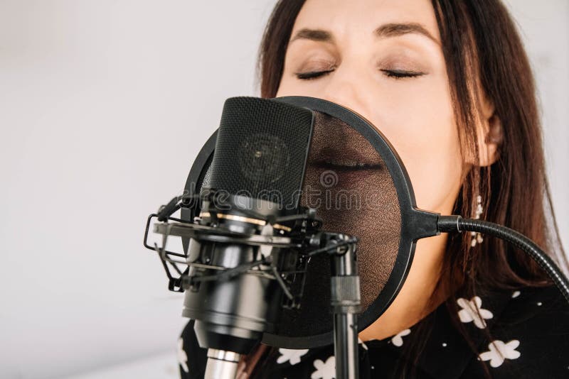 Porträtt av en vacker kvinna sjunger en låt nära en mikrofon i en inspelningsstudio Nära ansikte royaltyfri foto Porträtt av en vacker kvinna sjunger en låt nära en mikrofon i en inspelningsstudio Nära ansikte royaltyfri foto