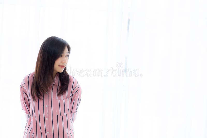 Porträtt av en vacker ung asiatisk kvinna som stod i fönstret och lekte medan hon vaknade upp med soluppgång på morgonen royaltyfri fotografi Porträtt av en vacker ung asiatisk kvinna som stod i fönstret och lekte medan hon vaknade upp med soluppgång på morgonen royaltyfri fotografi