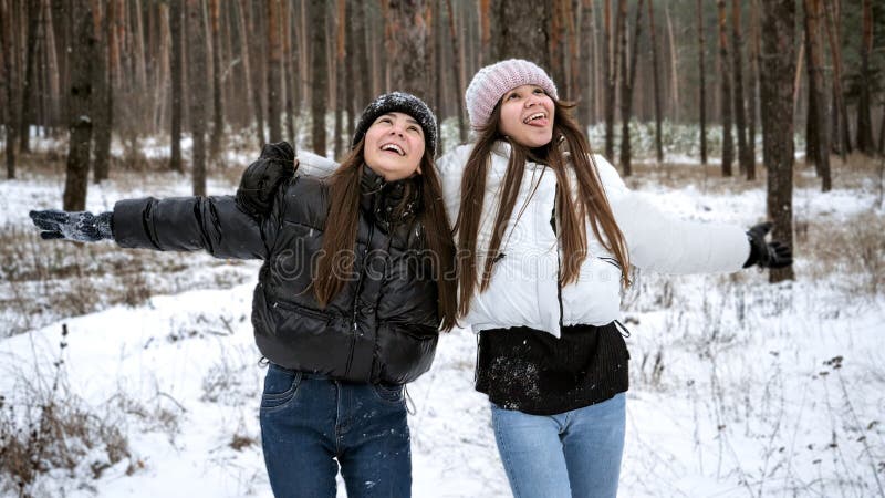 Porträtt av glada skrattande tonårsflickor som njuter av snöfall i vinterskog arkivfoton