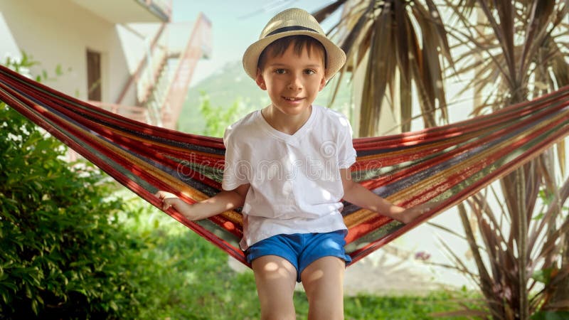 Porträtt av liten pojke som sitter i hammock och som simmar i trädgården. omsorgsfulla minnen från barndomen och avslappning av royaltyfria bilder