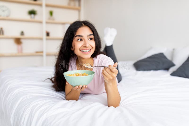 Porträtt av passande indian som äter spannmål med mjölk i sängen hemma och tar hand om kroppen fotografering för bildbyråer