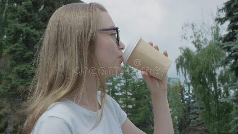 Porträtt av söt flicka med blonda hår och blå ögon som dricker från papp i kartong medan man tillbringar tid i parken på sommaren