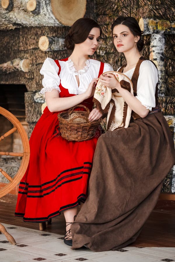 Porträtt av två underbara leende kaukasiska damer som pockar med snurrande hjul och fancykwork hoop in retro dress in rural enviro royaltyfri foto