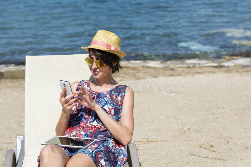 Porträtt av vacker ung kvinna med telefon på stranden fotografering för bildbyråer