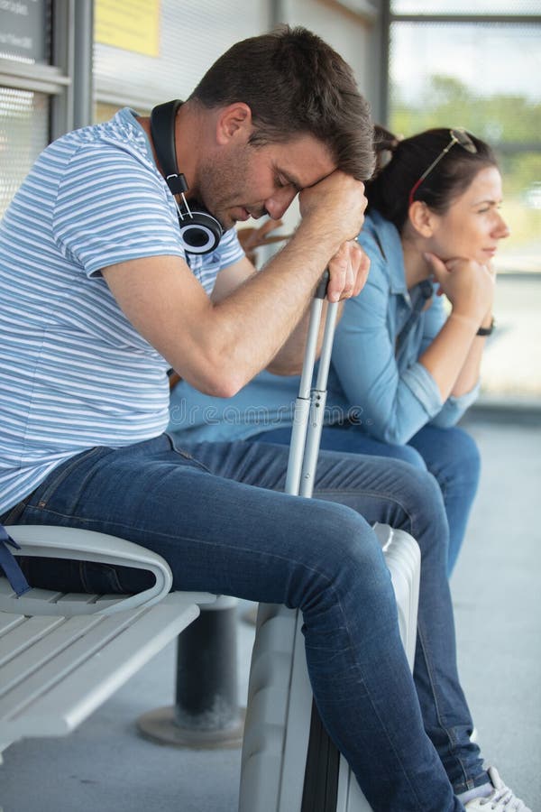 Porträtt par med bagage som sitter på bänk på stationen arkivbild