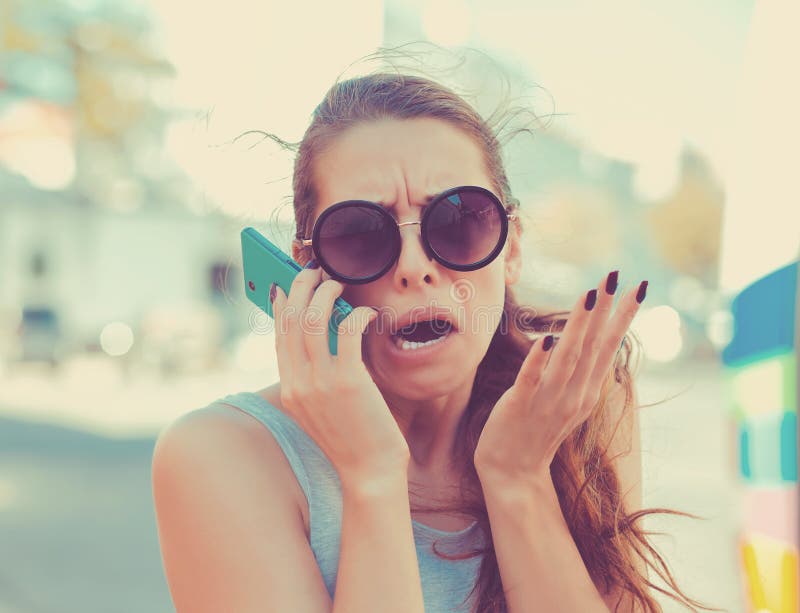 Portrait angry young woman screaming on mobile phone standing outside with city background. Negative emotions feelings. Portrait angry young woman screaming on mobile phone standing outside with city background. Negative emotions feelings.