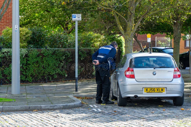 A traffic warden issuing a parking ticket on a parked car stock photography A traffic warden issuing a parking ticket on a parked car stock photography