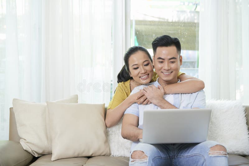 Portátil de observação de amor dos pares étnicos no sofá fotos de stock Portátil de observação de amor dos pares étnicos no sofá fotos de stock