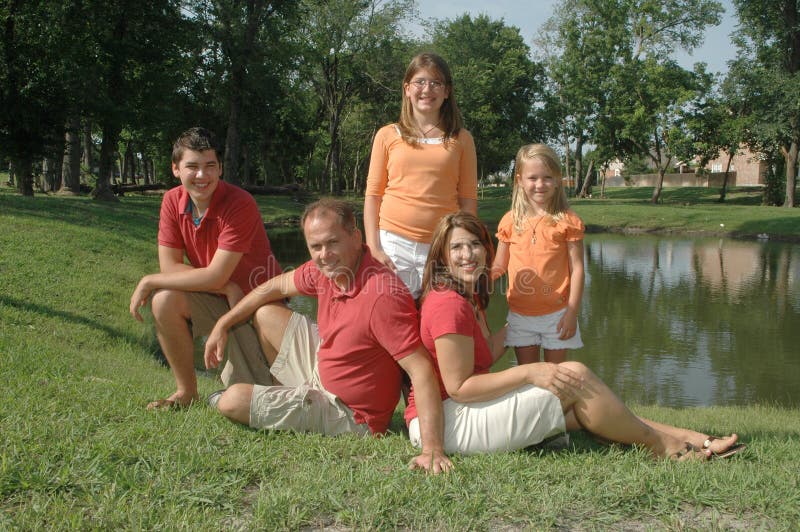 A lovely picture of a family of five, posing together at a public park next to a small pond. A lovely picture of a family of five, posing together at a public park next to a small pond.