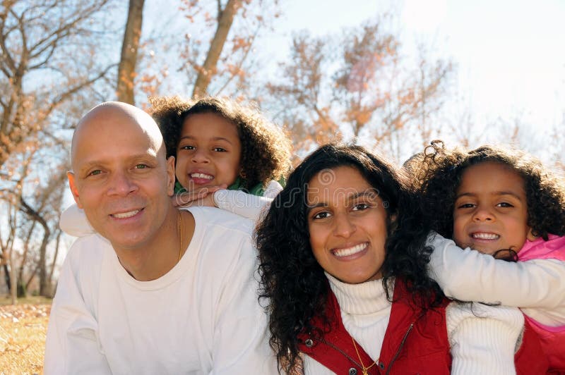 A multiracial family smiling and posing in a park setting. A multiracial family smiling and posing in a park setting.