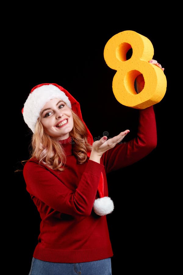 Positief meisje in een kostuum die van de Kerstmiskerstman een aantal acht op een zwarte achtergrond houden het concept van 2018 stock afbeelding Positief meisje in een kostuum die van de Kerstmiskerstman een aantal acht op een zwarte achtergrond houden het concept van 2018 stock afbeelding