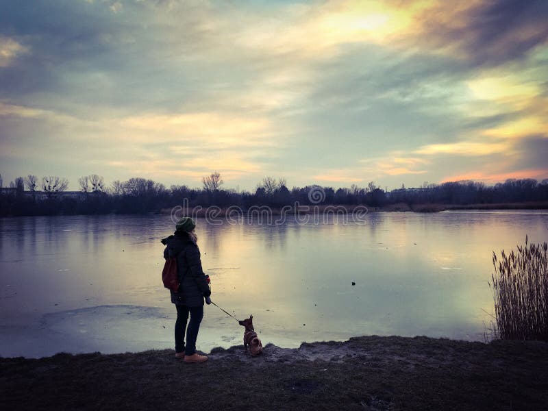 Position de femme avec son chien au bord de lac d'un lac congelé en hiver image stock Position de femme avec son chien au bord de lac d'un lac congelé en hiver image stock
