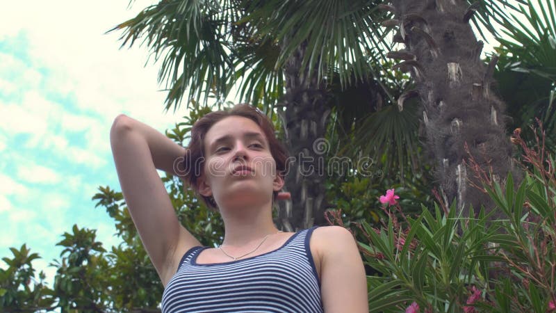 Position de jeune femme sur le remblai sous le palmier utilisant le rétro maillot de bain avec les rayures bleues et blanches