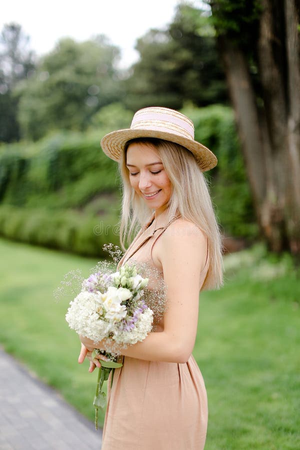 Position de jeune fille dans le yeard avec le bouquet des fleurs et du chapeau de port images stock Position de jeune fille dans le yeard avec le bouquet des fleurs et du chapeau de port images stock