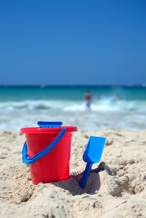 Red bucket and blue spade on sunny sandy beach on vacation or holiday. Red bucket and blue spade on sunny sandy beach on vacation or holiday