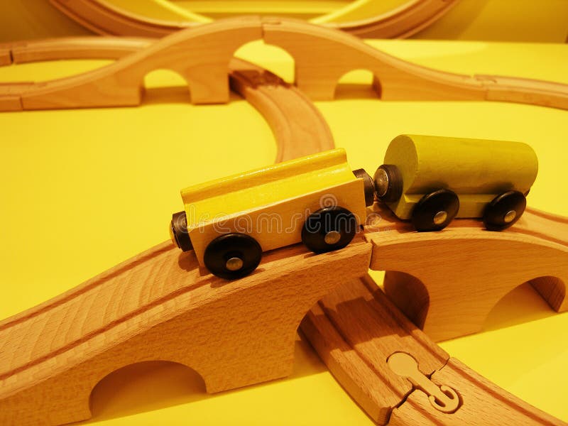 An image of a wood toy train set, with railway lines set up to form curved rail lines and bridges. Shown with two magnetic wagons of yellow and green. Simple and fun for children. Horizontal color format, nobody in picture. An image of a wood toy train set, with railway lines set up to form curved rail lines and bridges. Shown with two magnetic wagons of yellow and green. Simple and fun for children. Horizontal color format, nobody in picture.
