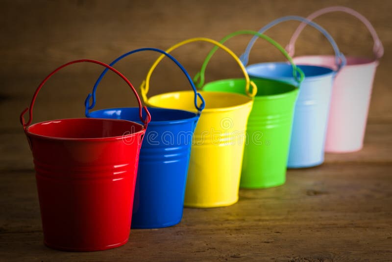 Five coloured buckets in one diagonal line on timber floor. Five coloured buckets in one diagonal line on timber floor