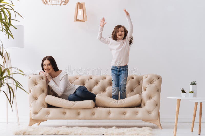 Positiv lycklig flickabanhoppning på soffan royaltyfri bild Positiv lycklig flickabanhoppning på soffan royaltyfri bild