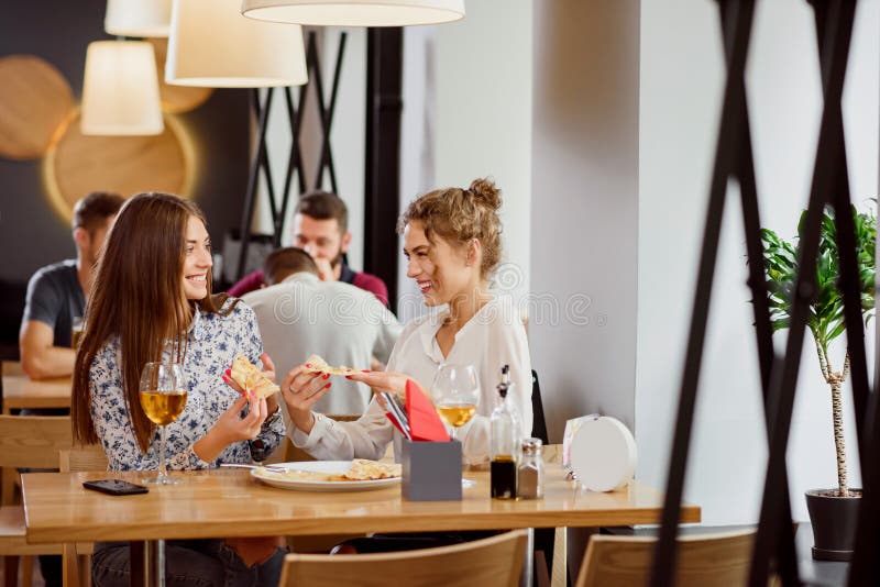 Positiva kvinnliga vänner som pratar och äter i pizzeria arkivbild Positiva kvinnliga vänner som pratar och äter i pizzeria arkivbild