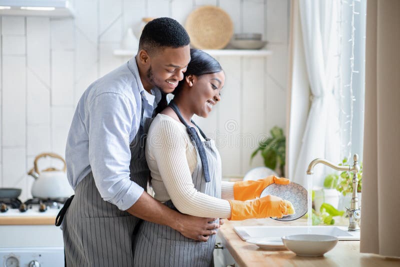 Positive Black Man Embracing His Wife While She Is Washing Dishes At Home Blank Space Stock