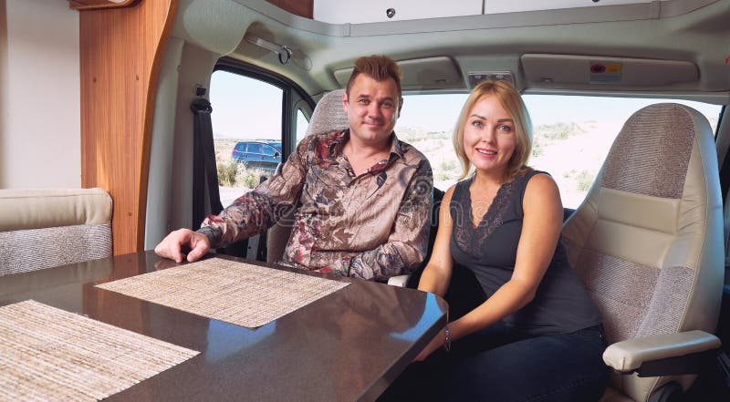 Positive couple sitting inside of recreational vehicle looking at camera