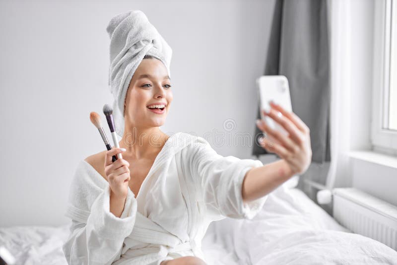 positive excited female take photo on smartphone, holding make-up brushes