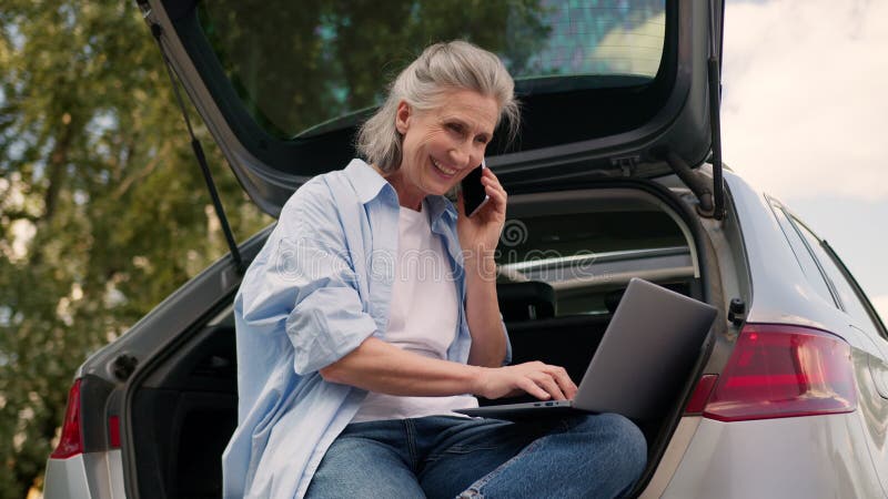 Positive glückliche kaukasische Senior frohe Geschäftsfrau Frau ältere Geschäftsfrau Freelancer sitzen offen Auto Kofferraum stock footage