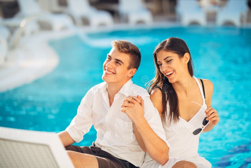 Positive happy couple relaxing by the swimming pool in luxury summer vacation resort.Enjoying time together in spa wellness center