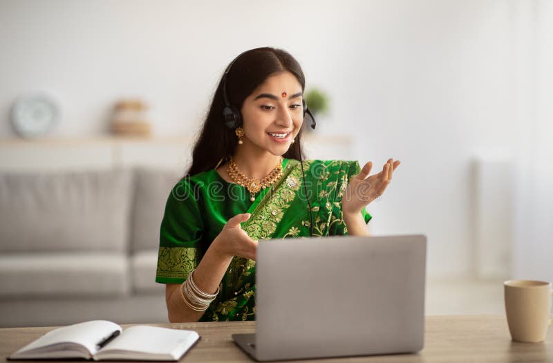 Positive indische Frau in traditionellen Sari Kleid tragen Kopfhörer mit Online-Treffen auf Laptop zu Hause