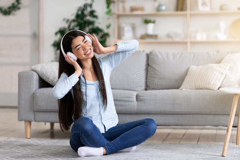 Positive korean girl enjoying music in wireless headphones while relaxing at home