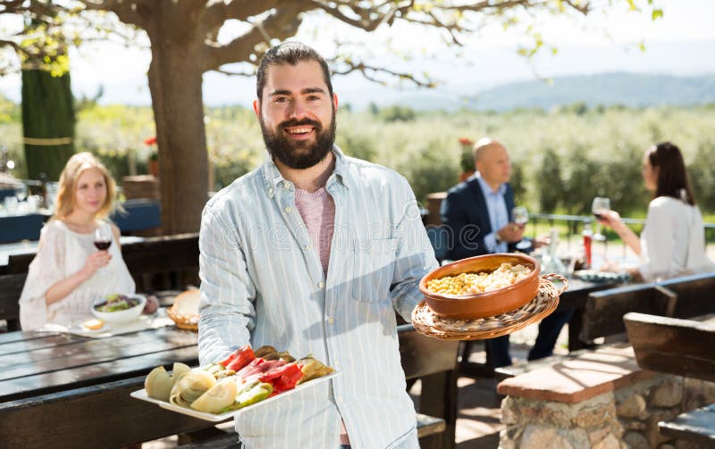 Positive Male Waiter Welcoming Guests To Country Outdoor Restaurant