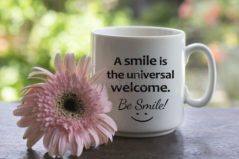 Positive message on a white coffee cup - A smile is the universal welcome. Be smile! with a happy smiling sign on it and a flower. stock photo