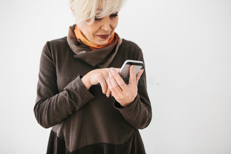 A positive modern elderly woman is holding a cell phone and is using it. The older generation and modern technology. stock image A positive modern elderly woman is holding a cell phone and is using it. The older generation and modern technology. stock image