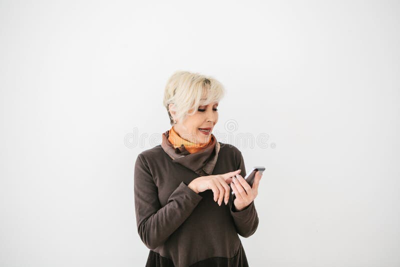 A positive modern elderly woman is holding a cell phone and is using it. The older generation and modern technology. stock photography A positive modern elderly woman is holding a cell phone and is using it. The older generation and modern technology. stock photography
