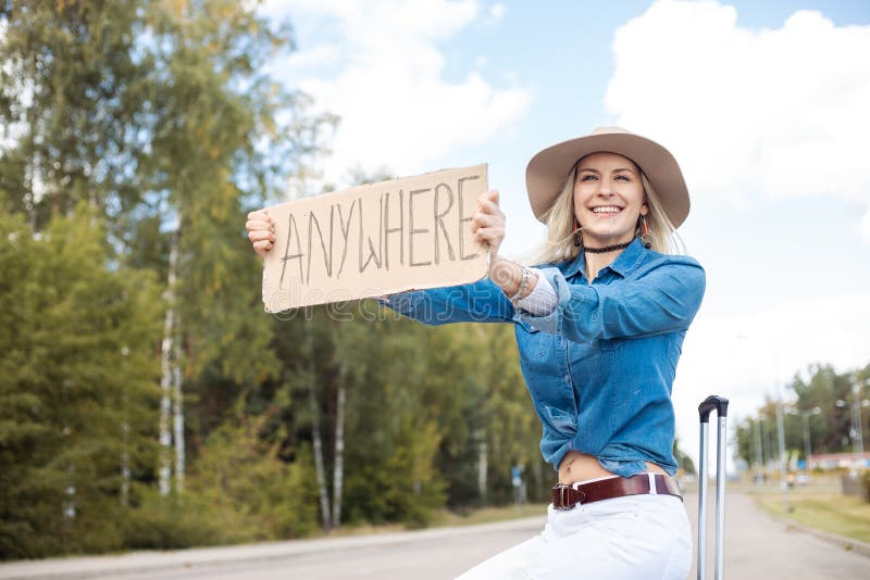 Positive Smiling Carefree Blond Woman Hitchhiking Attract Attention By Road With Cardboard