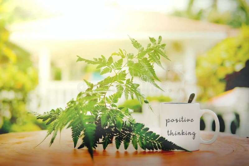 Positive thinking words written at white mug on the wooden table against leaf and sun flare with blurry bokeh background