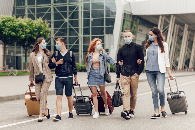 Positive young people in protective masks with luggage outdoor near the airport. Young students return home stock photo Positive young people in protective masks with luggage outdoor near the airport. Young students return home stock photo