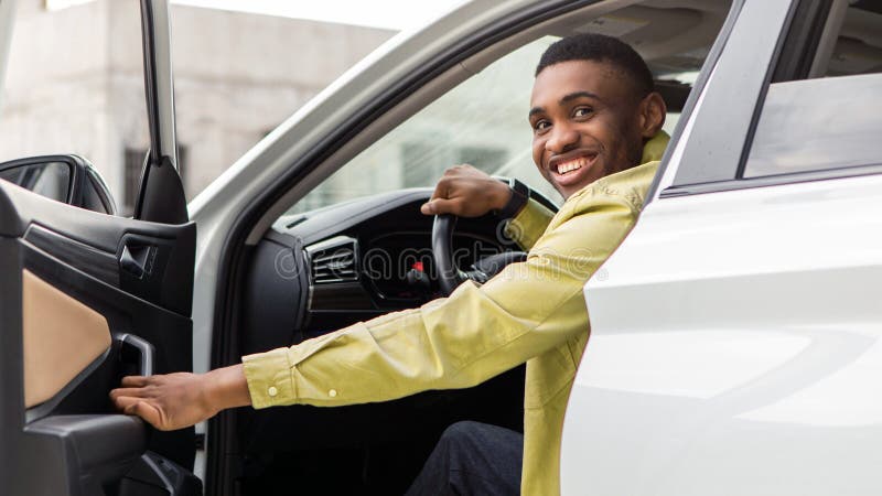Positiver schwarzer Mann, der aus dem Auto rausgeht, öffnet Autotür und lächelt hinein. Auto-Testlaufbuchung lizenzfreies stockbild