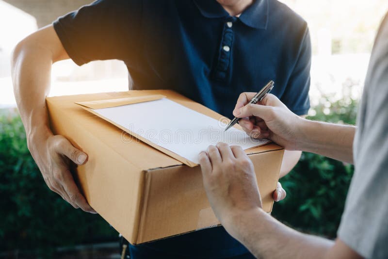Posição do homem novo da entrega na porta da casa e de pacotes levando para o homem novo à assinatura foto de stock Posição do homem novo da entrega na porta da casa e de pacotes levando para o homem novo à assinatura foto de stock