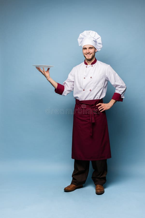 Posição masculina feliz do cozinheiro do cozinheiro chefe com a placa isolada em claro - fundo azul foto de stock royalty free Posição masculina feliz do cozinheiro do cozinheiro chefe com a placa isolada em claro - fundo azul foto de stock royalty free