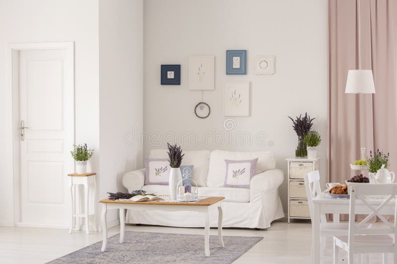 Posters above white sofa in spacious flat interior with flowers on table near door. Real photo concept